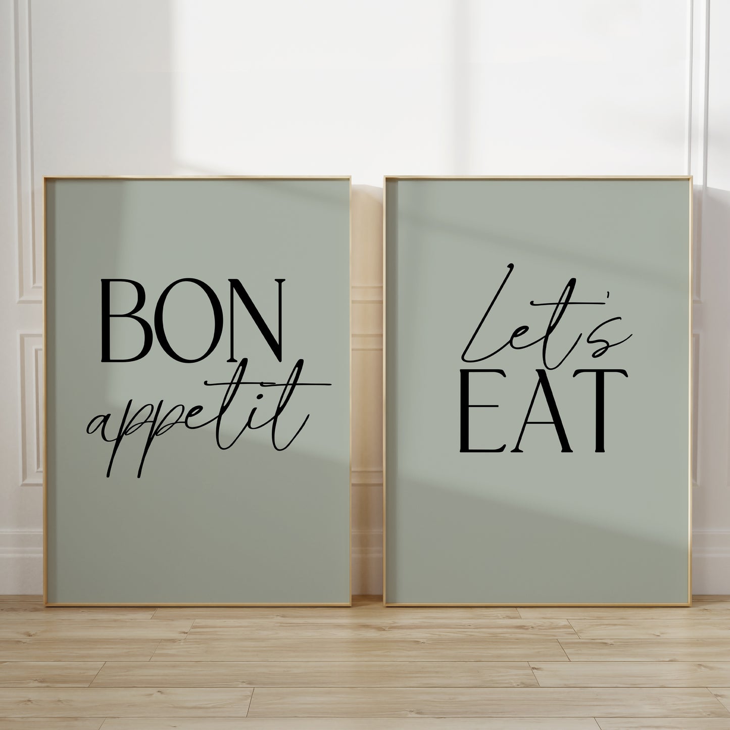Two unframed vertical kitchen wall art prints in sage green. The left print says “BON appetit” in black lettering on a pale sage green background, and the right print says “Let’s EAT” in black lettering on the same pale sage green background.