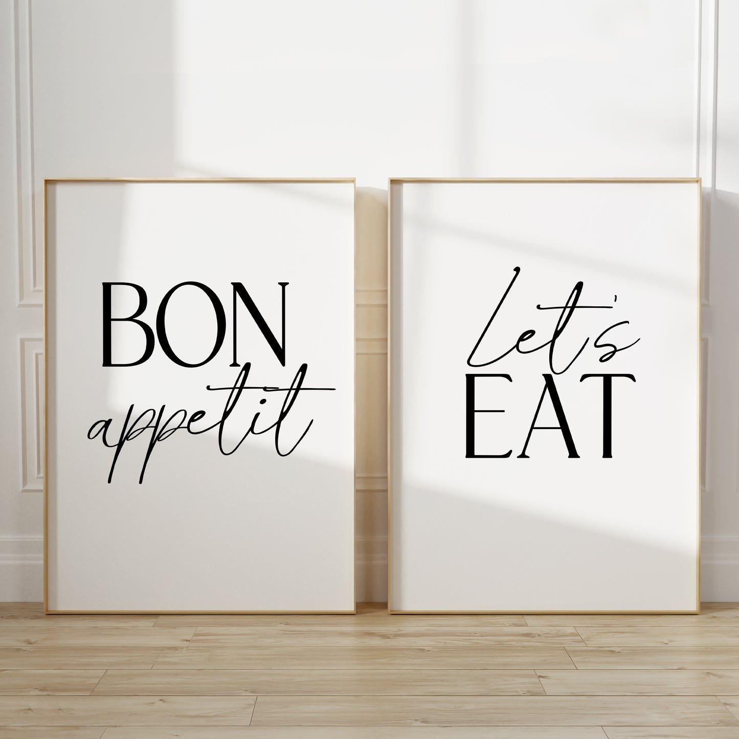 Two kitchen wall art prints. The left print says “BON appetit” in black lettering, and the right print says “Let’s EAT” in black lettering, both on white backgrounds.
