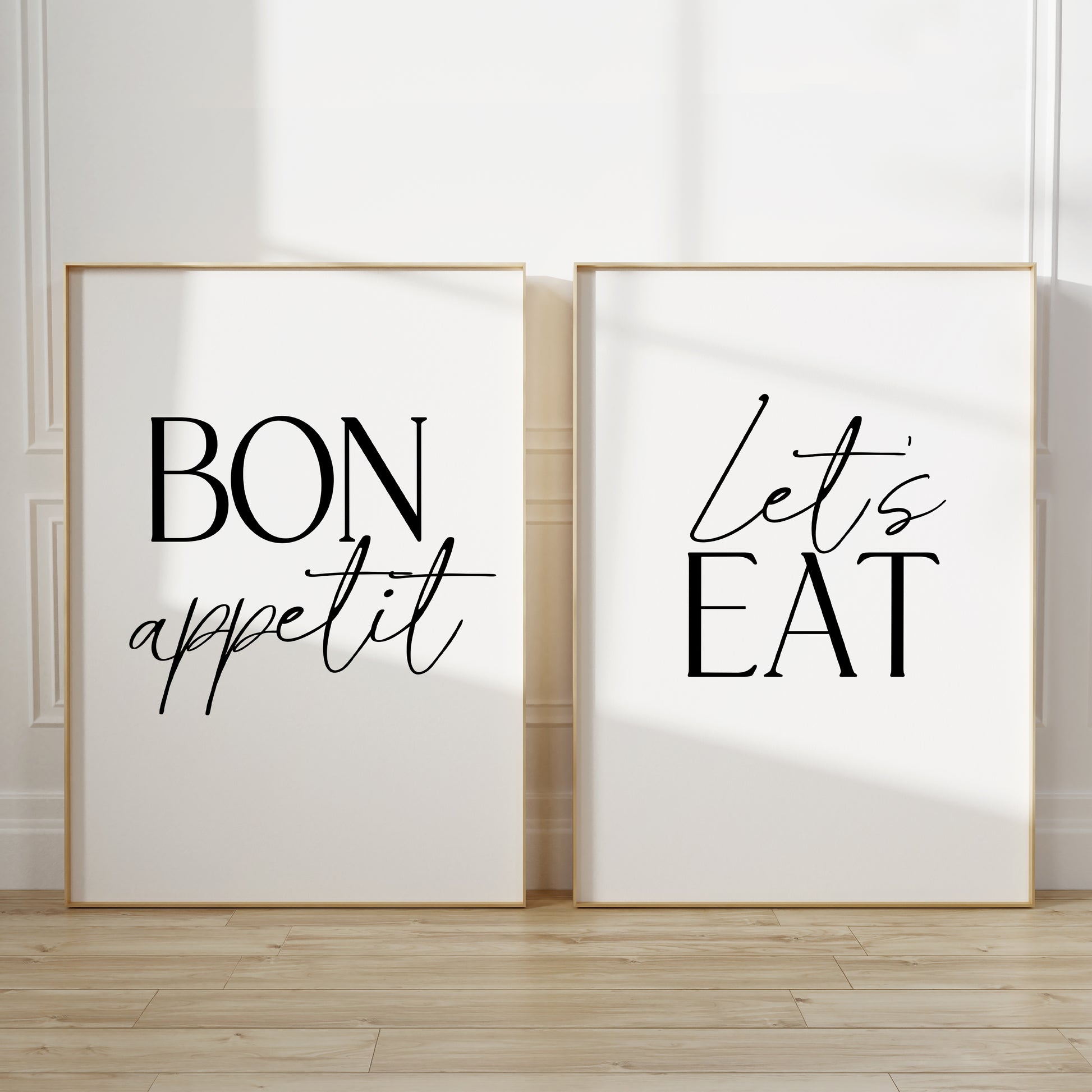 Two kitchen wall art prints. The left print says “BON appetit” in black lettering, and the right print says “Let’s EAT” in black lettering, both on white backgrounds.