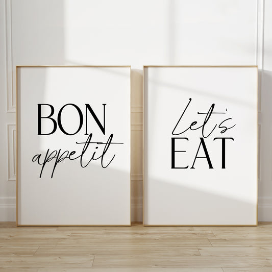 Two kitchen wall art prints. The left print says “BON appetit” in black lettering, and the right print says “Let’s EAT” in black lettering, both on white backgrounds.