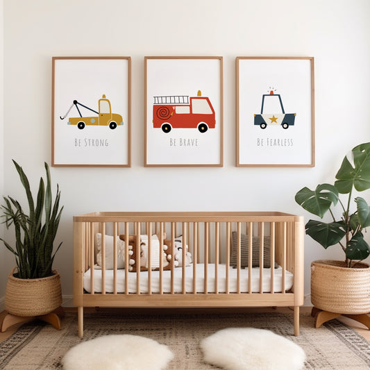 A set of three wall prints featuring various vehicles and the phrases 'BE STRONG', 'BE BRAVE', and 'DON'T TEAR IT' displayed in a nursery room setting with a wooden crib and a green plant.