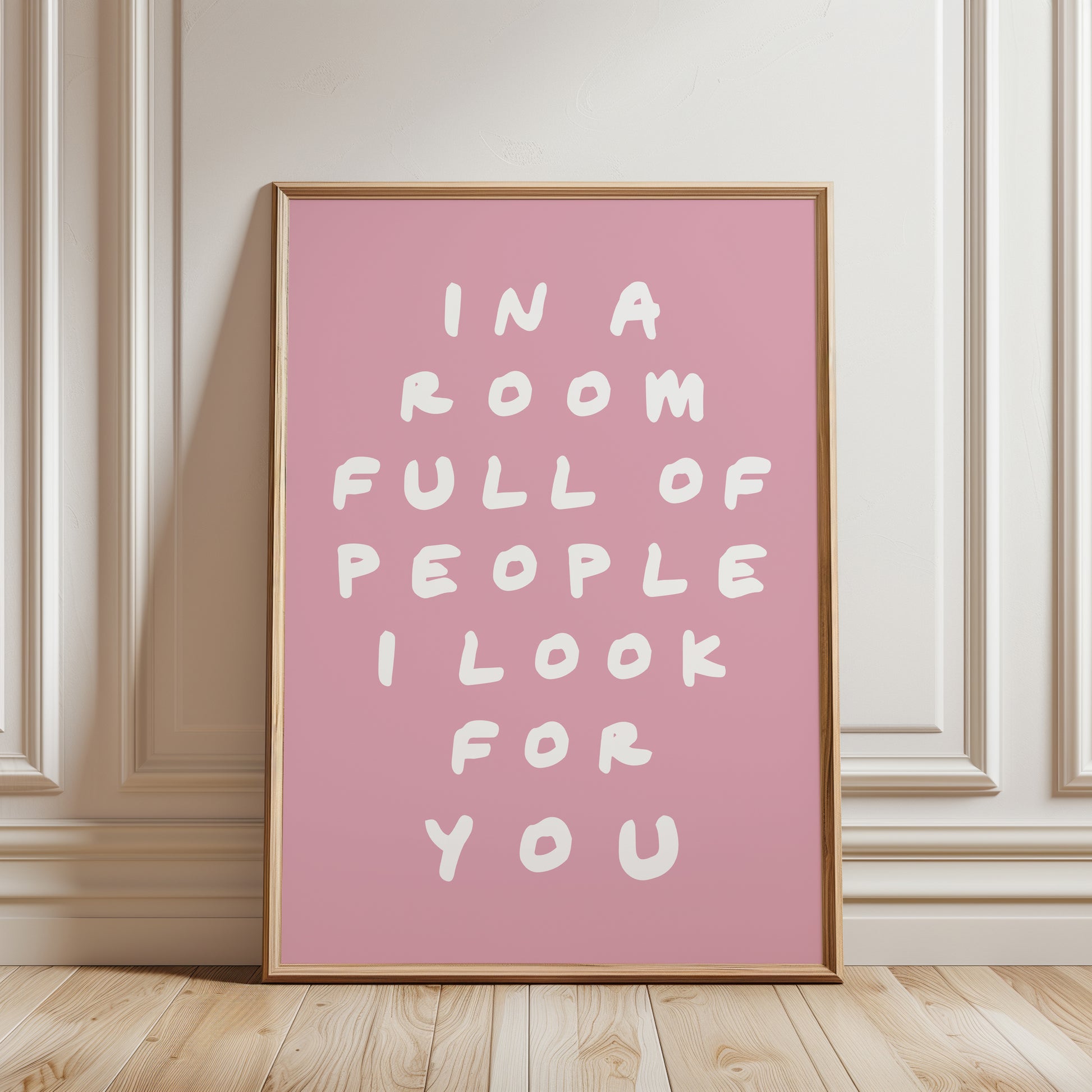 An unframed typographic wall art print. The print has white hand-drawn text reading “IN A ROOM FULL OF PEOPLE I LOOK FOR YOU” on a  pink background.