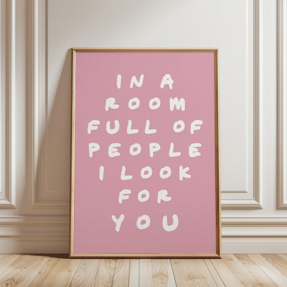 An unframed typographic wall art print. The print has white hand-drawn text reading “IN A ROOM FULL OF PEOPLE I LOOK FOR YOU” on a  pink background.