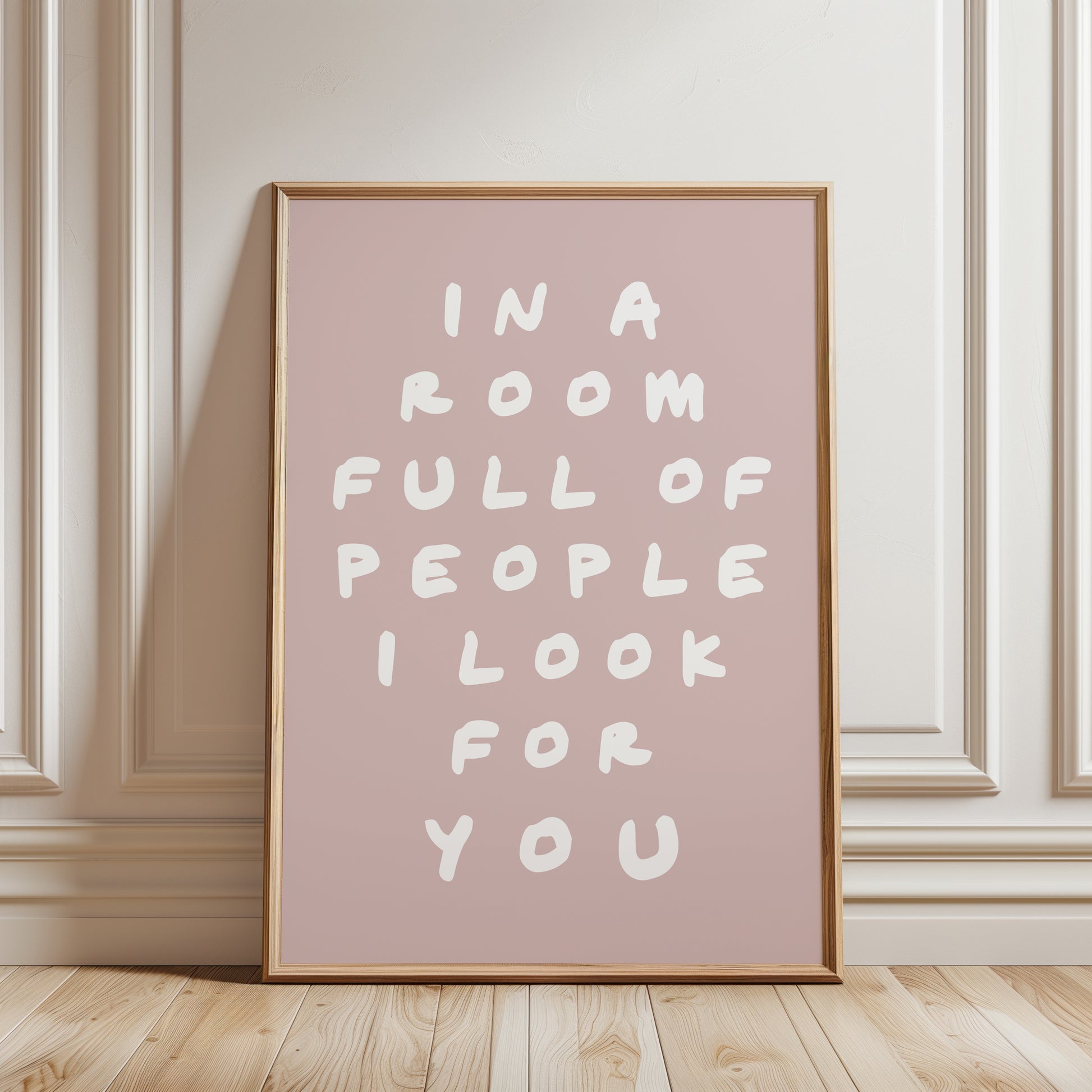 An unframed typographic wall art print. The print has white hand-drawn text reading “IN A ROOM FULL OF PEOPLE I LOOK FOR YOU” on a nude pink background.