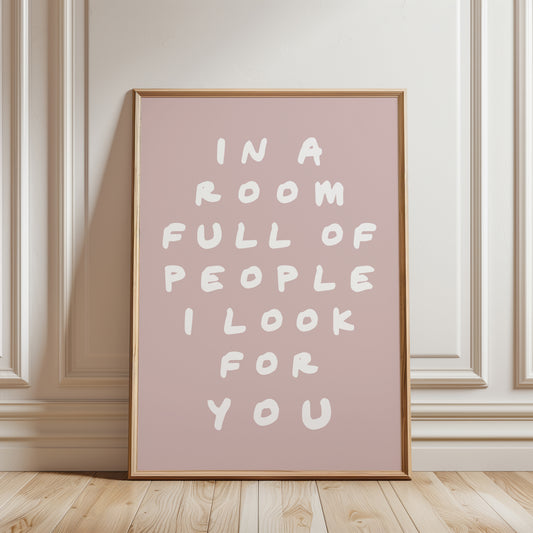 An unframed typographic wall art print. The print has white hand-drawn text reading “IN A ROOM FULL OF PEOPLE I LOOK FOR YOU” on a nude pink background.