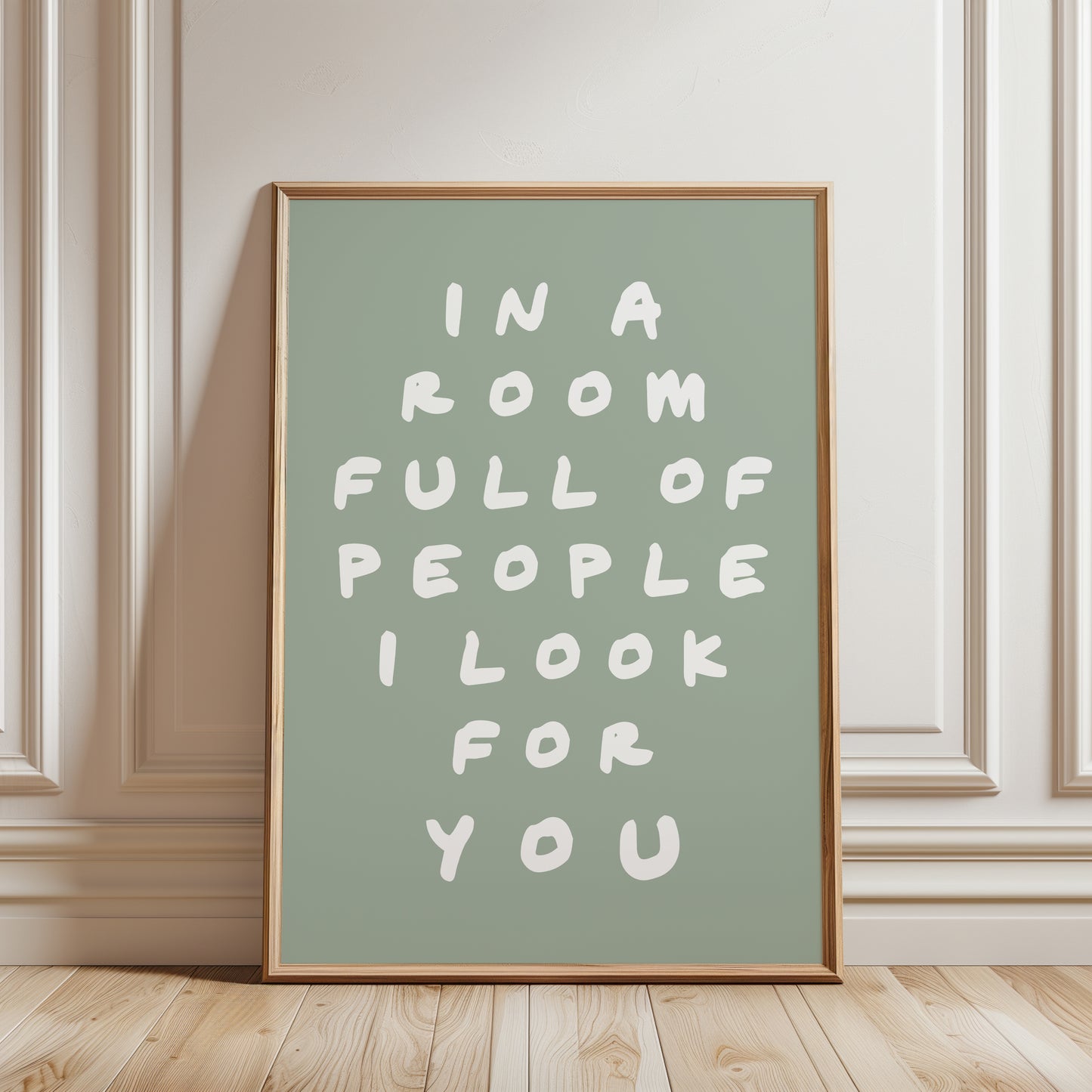 An unframed typographic wall art print. The print has white hand-drawn text reading “IN A ROOM FULL OF PEOPLE I LOOK FOR YOU” on a  sage green background.